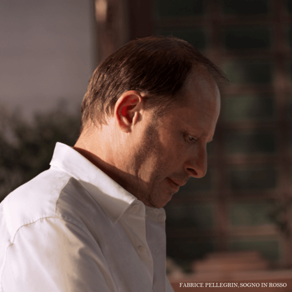 A man in a white shirt stands in profile, looking down thoughtfully, with soft lighting highlighting his features.