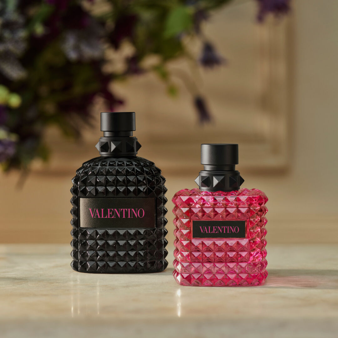 Two Valentino perfume bottles, one pink and one black, featuring a textured, pyramid-studded design on a neutral background.