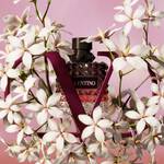 A stylish perfume bottle surrounded by white flowers and framed by a stylized "V" shape, set against a soft pink background.