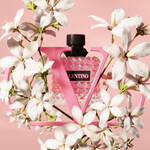 A pink Valentino perfume bottle surrounded by white flowers against a soft pink background.