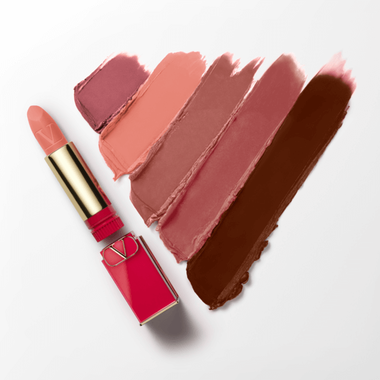 A vibrant pink lipstick in a gold and pink case, positioned next to its stylish packaging on a soft white surface.