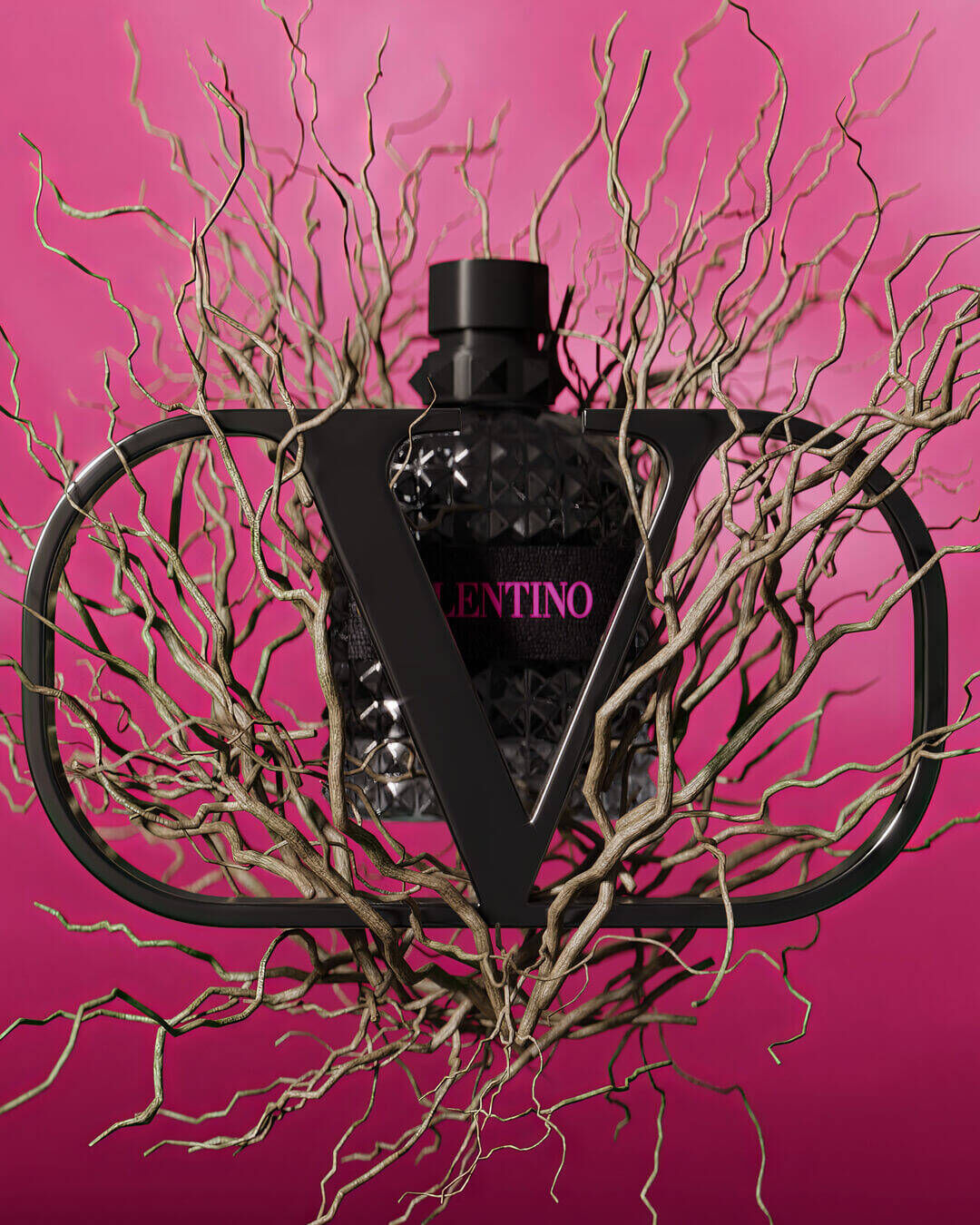 A black diamond-patterned perfume bottle is encased in a black frame shaped like the letter "V," surrounded by twisted, bare branches against a vibrant pink background.